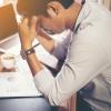 Stressed-out man sits at desk with face in hands