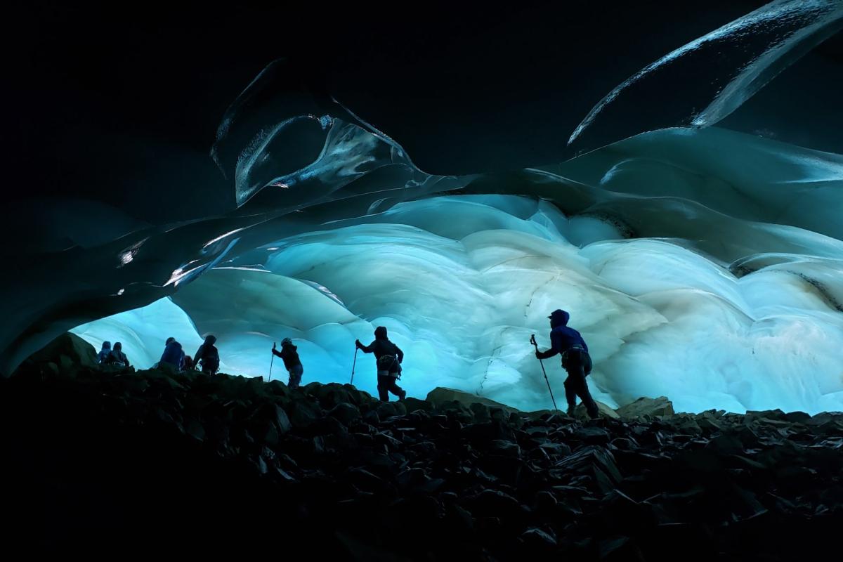 A photo of hikers at night in front of a cave of ice