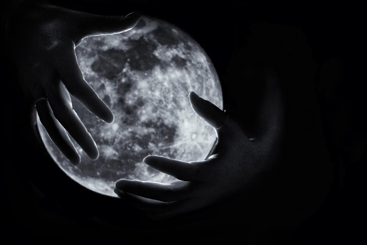 A black-and-white photo of a person's hands partiallly covering the moon
