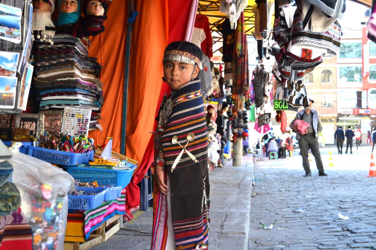 A photo of a boy in a market with colorful blankets