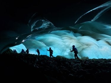 A photo of hikers at night in front of a cave of ice