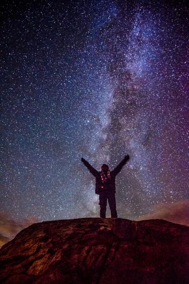 A photo of a man with raised arms under a starry night sky