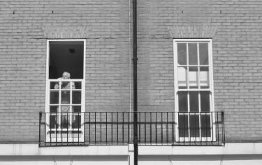 A black-and-white photo of a man standing at his window