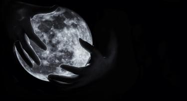A black-and-white photo of a person's hands partiallly covering the moon