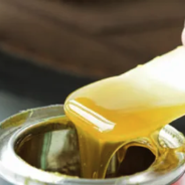 A hand scoops a syrup-like substance out of a small metal can.