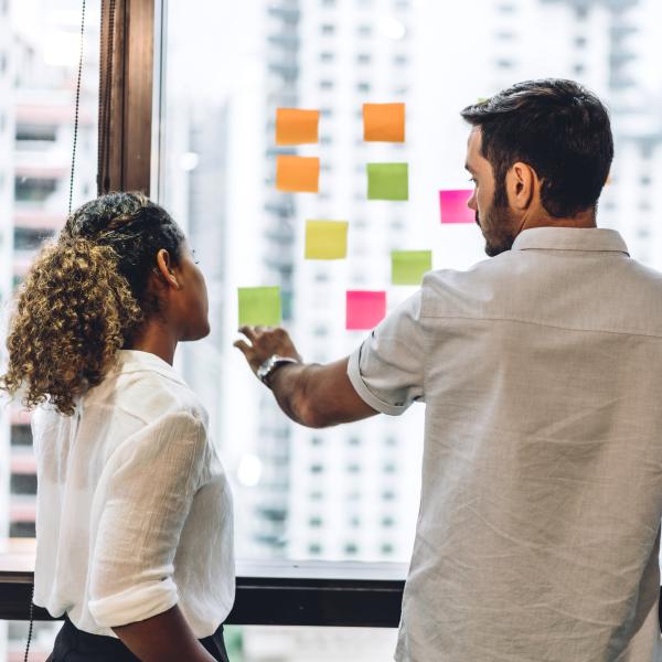 Two white men and a woman of color work on a strategy with sticky notes on a winodw