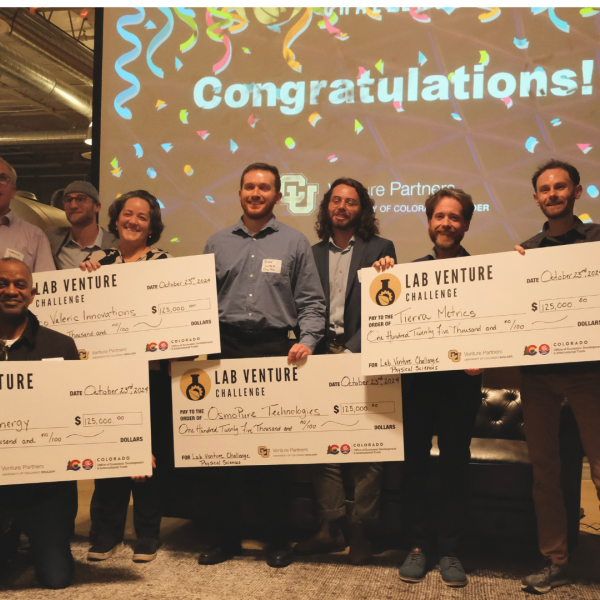 A diverse group of people stand with five giant prize checks as the confetti falls.