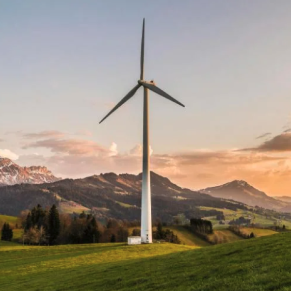 A loan modern windmill with a sunset in the mountains behind it