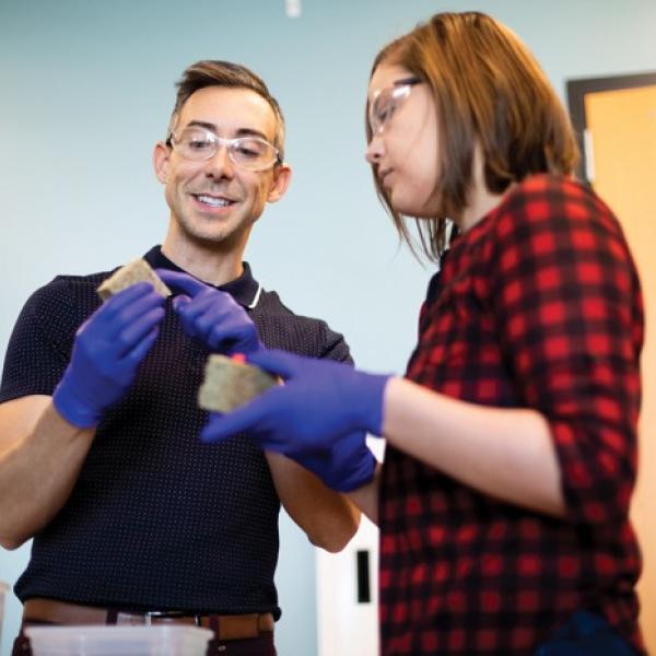 Wil Srubar and student Sarah Williams discuss the block-like materials they are holding in a laboratory.