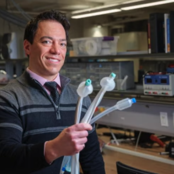 A man stands in a lab and holds up three tubular devices