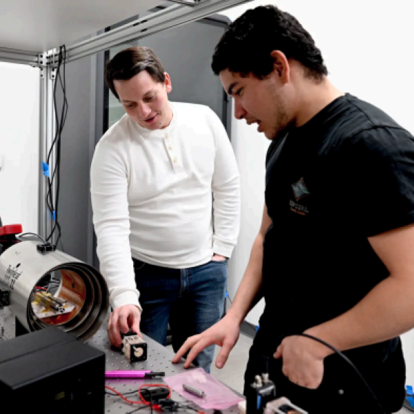 Two men work on a mechanical device in a laboratory
