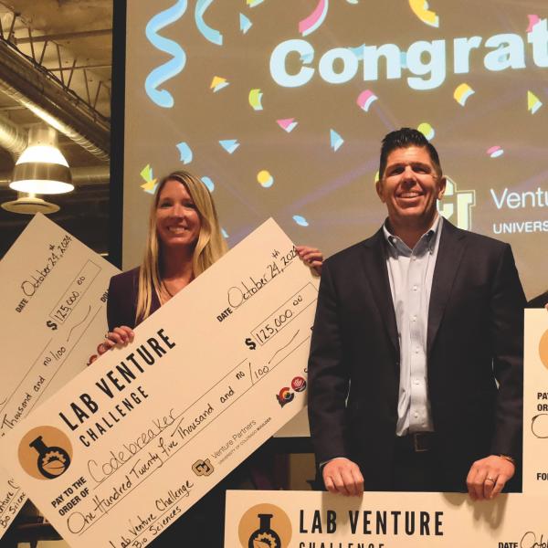 A diverse group of people stand together with giant prize checks.