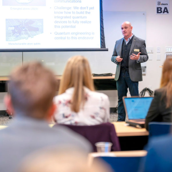 A man stands and gives a presentation to a group of people in a classroom