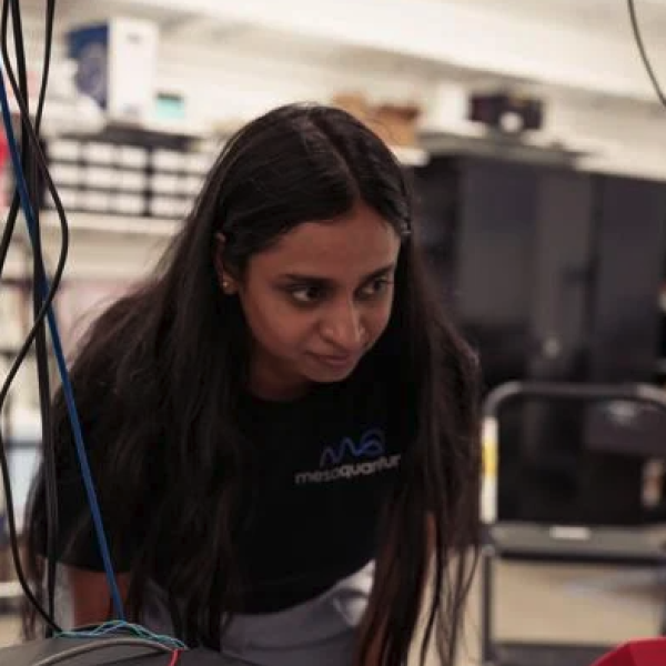 A woman stands over a workshop table covered with wires and machinery