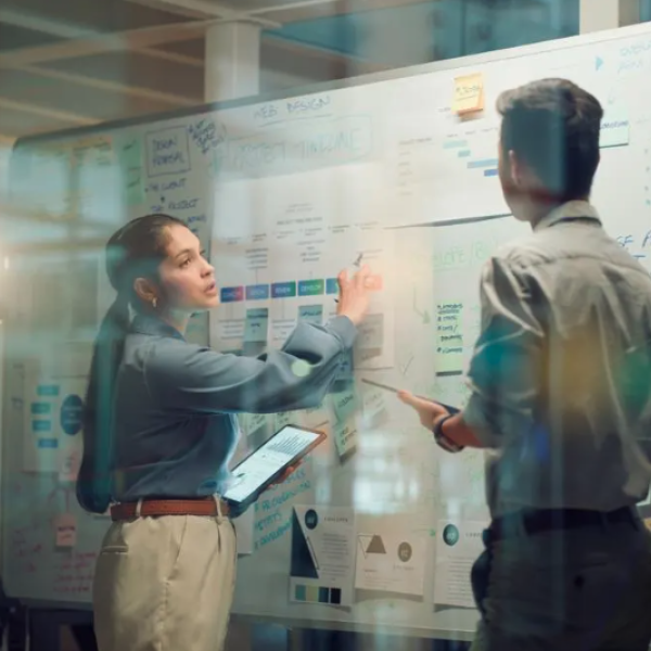 Two people stand at a white board planning something complex