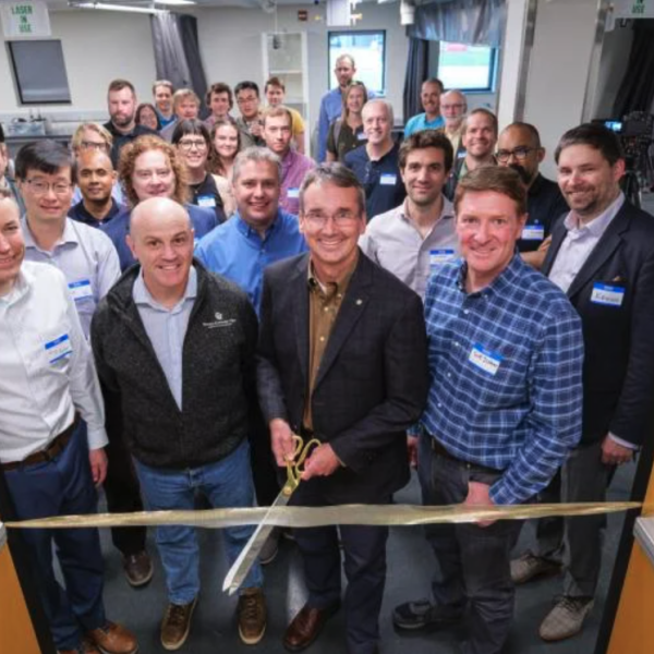 A group of predominantly white men stand at a ribbon cutting in the entrance of a laboratory