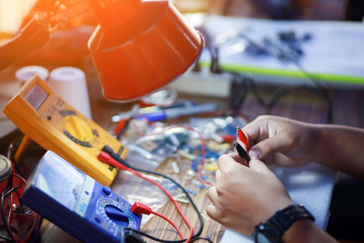Close up on hands working with a voltameter at a workshop table.