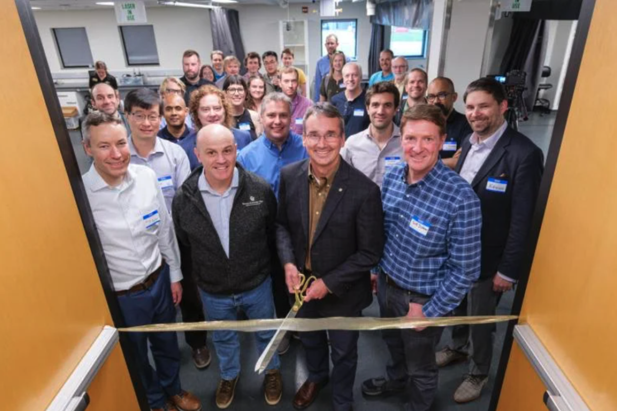 A group of predominantly white men stand at a ribbon cutting in the entrance of a laboratory