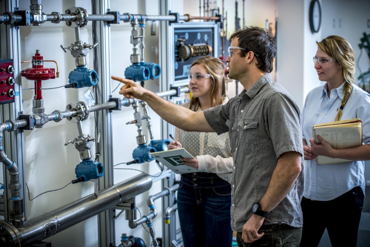 Two women and a man work together on a complex system of pipes.