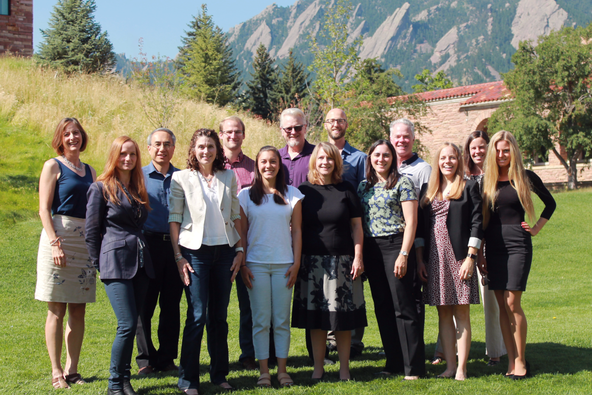 A group of men and women standing on the CU Boulder campus in front of the Boulder Flatirons