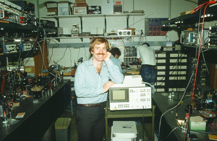 A man stands in a lab surrounded by complicated computer equipment