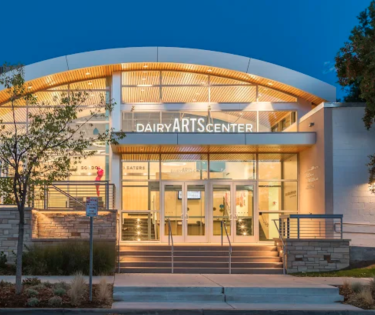 The all glass entrance to a warmly lit, whimsical building at dusk