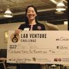 An asian woman smiles and holds up a giant prize-winning check for $125,000