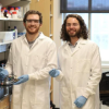 Two men in white lab coats stand together in a research lab