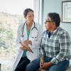 A woman doctor meets with a masculine-presenting person in a plaid shirt.
