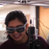 A man in business clothes works with two young woman in a lab.