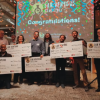 A diverse group of peoples stands together with five giant prize checks