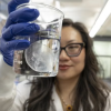 A woman in a lab holds up a beaker with a jelly fish inside it