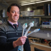 A man stands in a lab and holds up three tubular devices