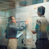 Two people stand at a white board planning something complex
