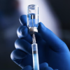 A hand wearing gloves fills a syringe from a bottle of liquid