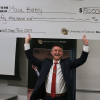 Grinning man stands with a giant check for $50,000 held over his head