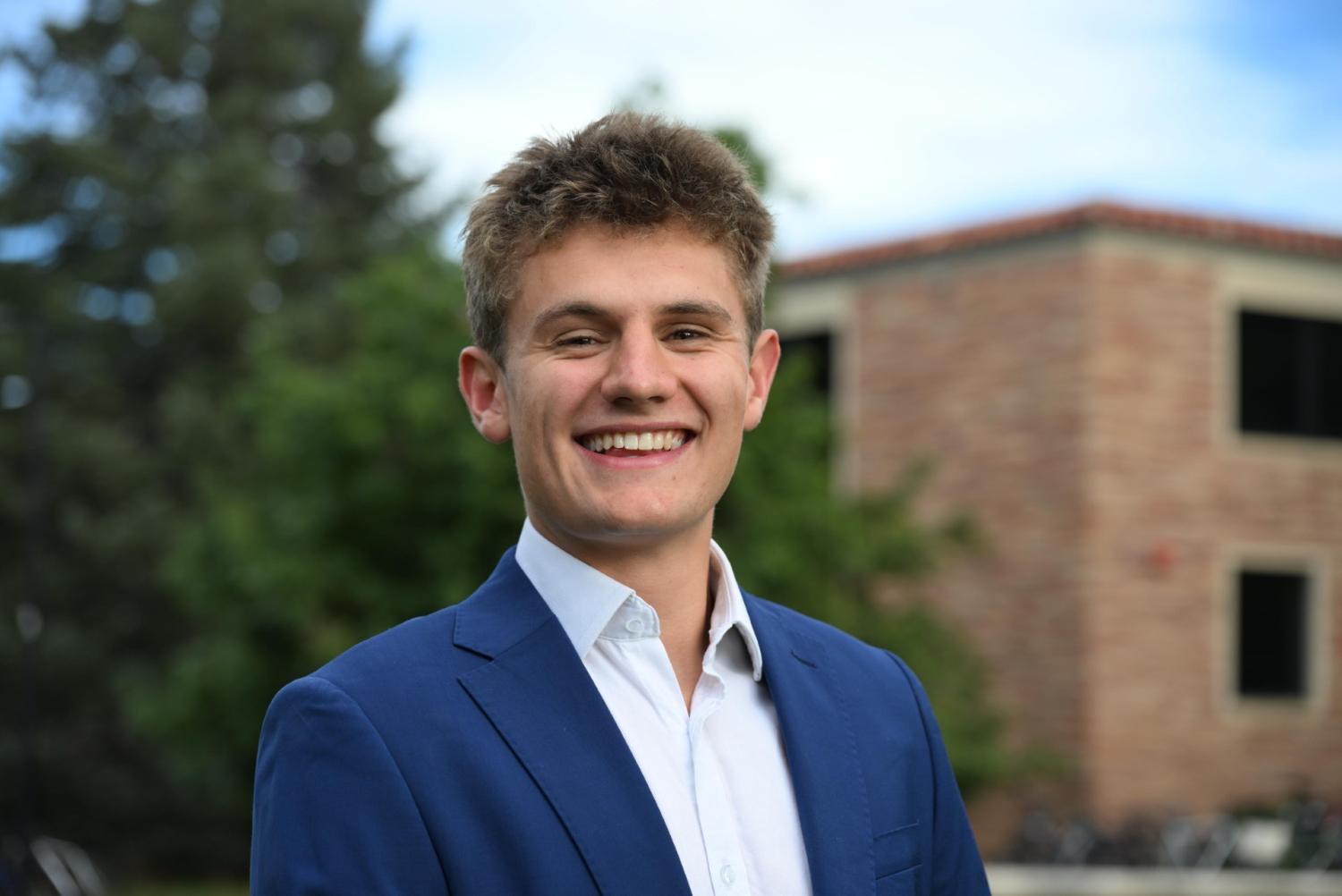 Man smiles in front of building and tree