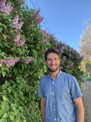 Jacob hall in a blue short-sleeved shirt standing next to pink flowers