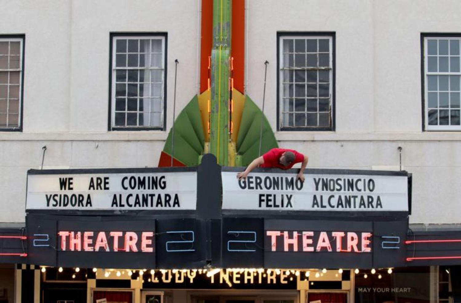 Marquise Theatre Headliner awning is pictured with a person in a red shirt standing above the awning, placing letters "We are Coming Ysidora Alcantara Geronimo Ynosincio Felix Alcantara"