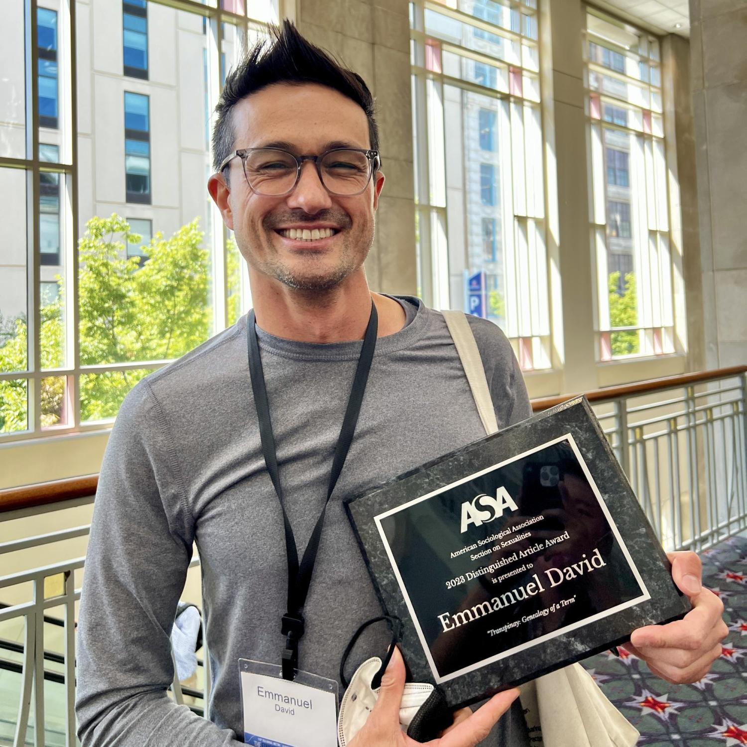 Dr. Emmanuel David smiles widely while holding the physical award plaque for the 2023 Distinguished Article Award from the ASA